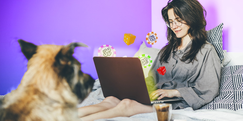 MUJER JOVEN ACOSTADA EN SU CAMA JUNTO A SU PERRO MIENTRAS ELLA DE IGUAL MANERA TIENE SU COMPUTADORA Y ESTÁ JUGANDO EN PLAYUZU MUY ENTRETENIDA