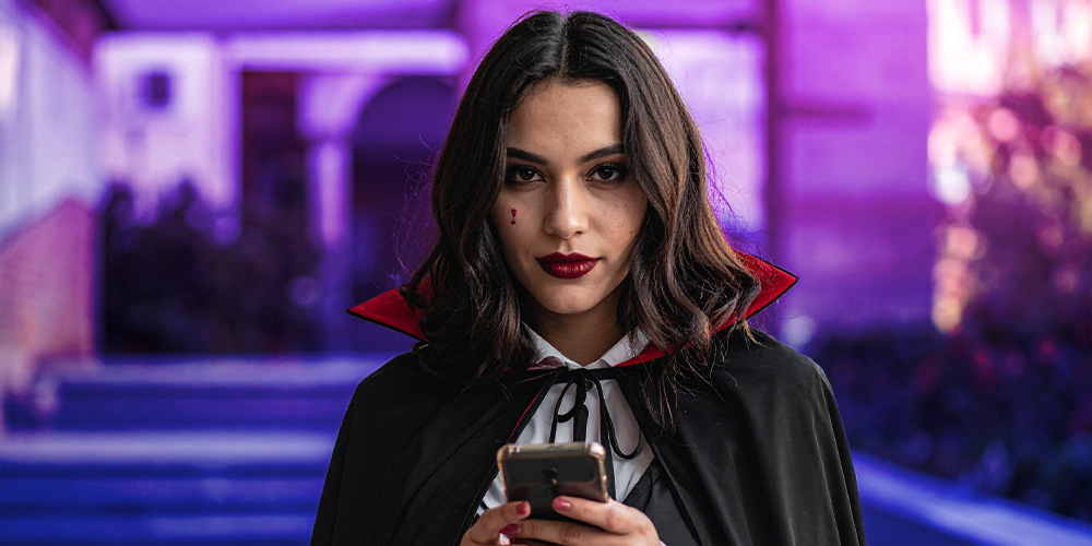 MUJER DE 20 AÑOS, LA CUAL ESTÉ DISFRAZADA DE DRÁCULA MIENTRAS ESTÁ VIENDO DE FRENTE CON SU TELÉFONO EN LA MANO, COMO SI ESTUVIERA ASUSTANDO DE FRENTE AL UZUARIO QUE ESTÉ LEYENDO EL BLOG