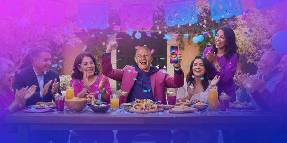 FACUNDO EN UNA MESA MUY GRANDE COMO SI ESTUVIERA COMIENDO CON UNA FAMILIA MEXICANA DISFRUTANDO EL DIA MIENTRAS TODOS EN LA MESA CELEBRAN YA QUE FACUNDO GANO EN PLAYUZU CON SU TELEFONO EN MANO